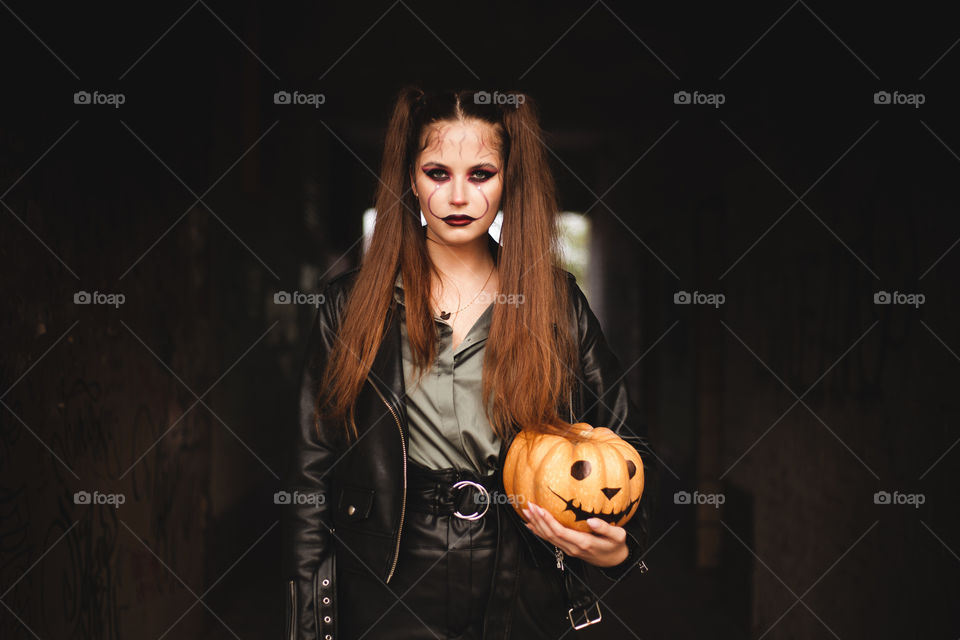 Young Woman holds a pumpkin in her hands. Painted pumpkin. Woman with bright makeup for Halloween. Halloween 2020. Place for inscription.