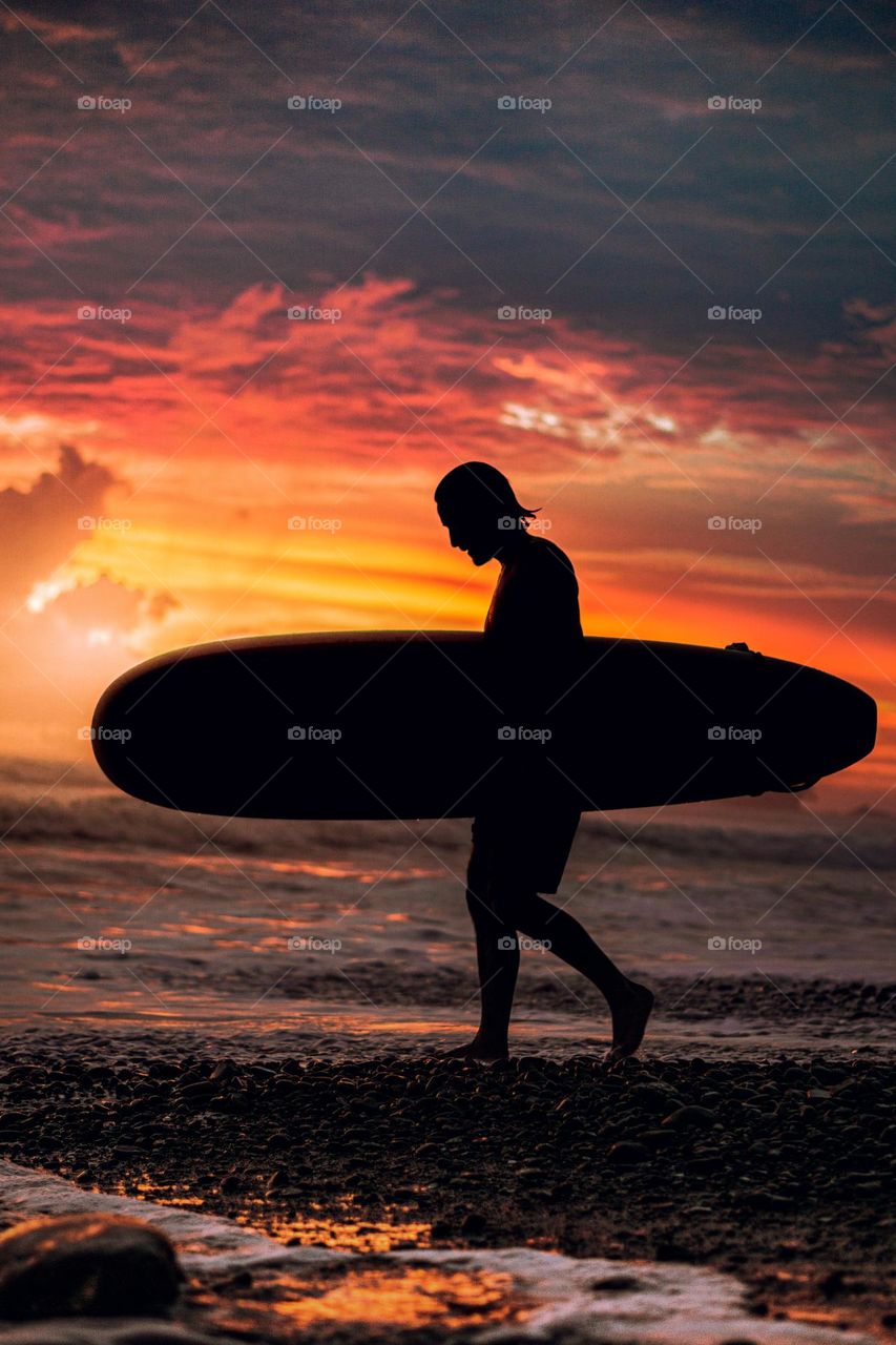 Beautiful sunset on the beach. Surfer walking towards the sea in a sunset