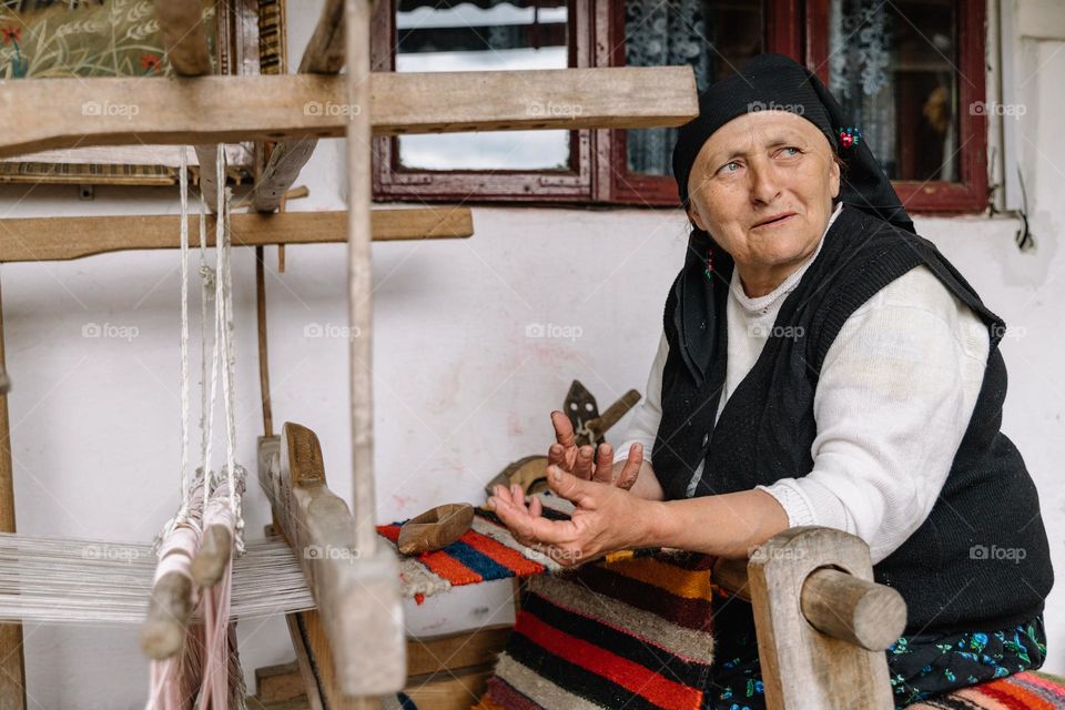 Elderly woman working at an traditional old loom, explaining how it’s functioning and how she learned to work at it.