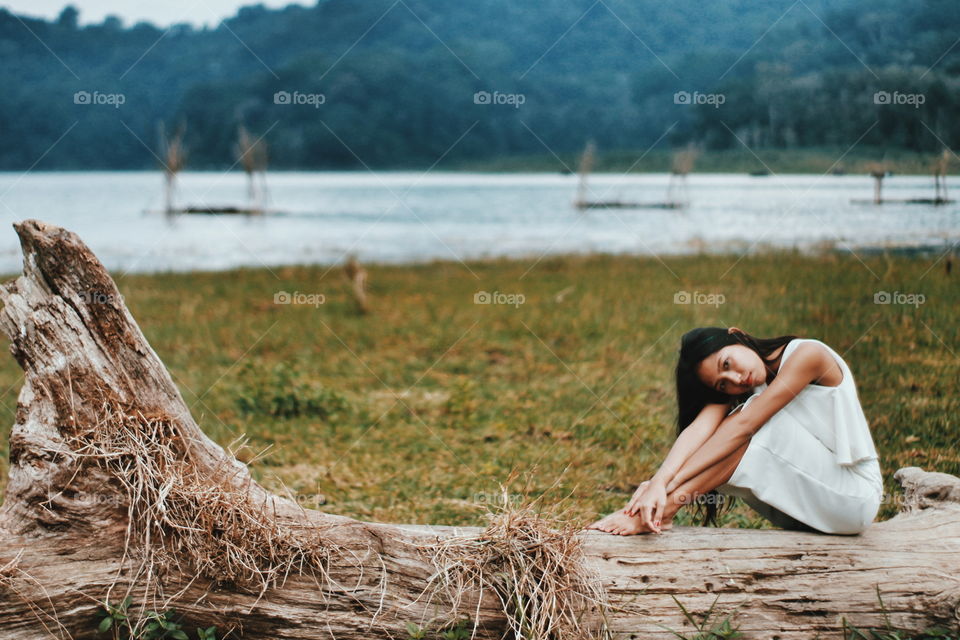 woman seating on thw dead tree on the lakesidd