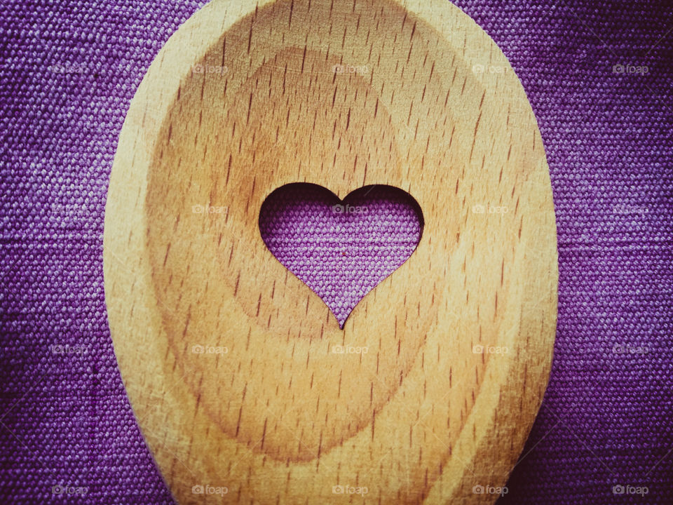 A wooden spoon with a heart in the middle of it on a purple background close up in macro