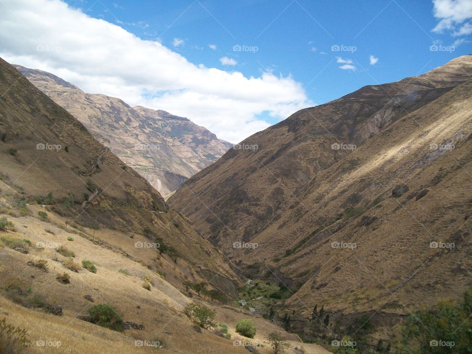 Deep scenic valley in Ecuador with dry brush down to a small stream meandering between the mountains