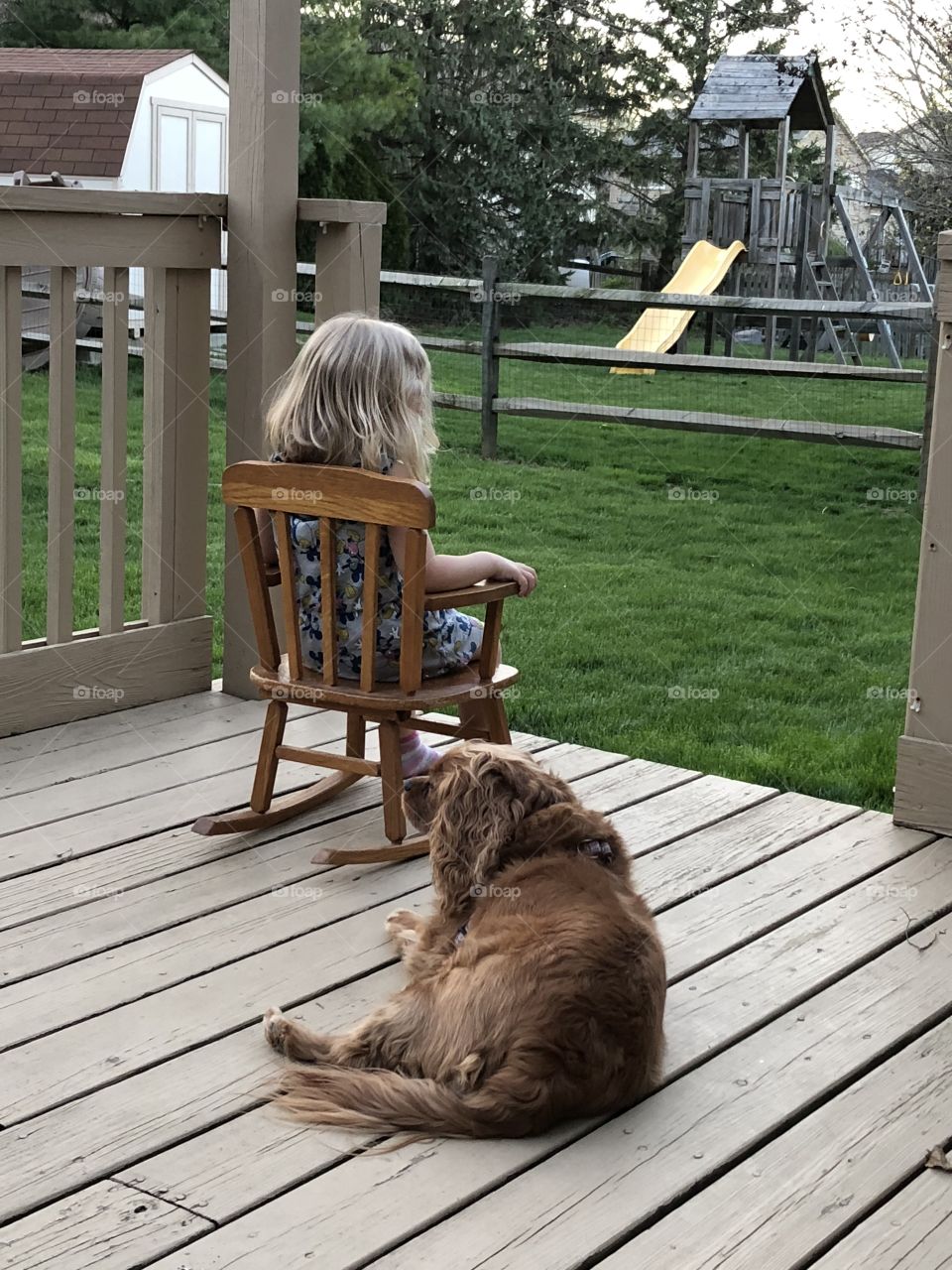 A little girl rocking on the porch with her loyal companion by her side.