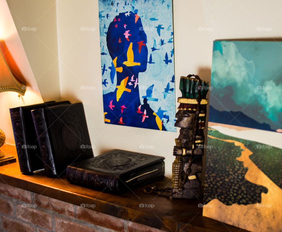Displate art inspiring travel and exploration next to leather bound books and travel souvenirs on rustic wood shelf on brick with antique lamp 