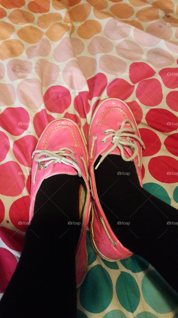 Girl wearing bright pink loafers shoes with black socks, on a pink bedspread.