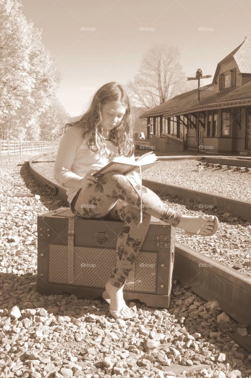 Young lady, reading a book, waiting on a train. 