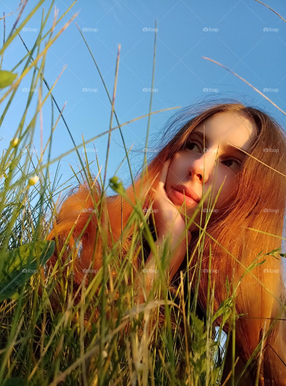 It is a photo of a young woman in the field. She has red (ginger) hair. She has brown eyes. It is a portarait on sky background