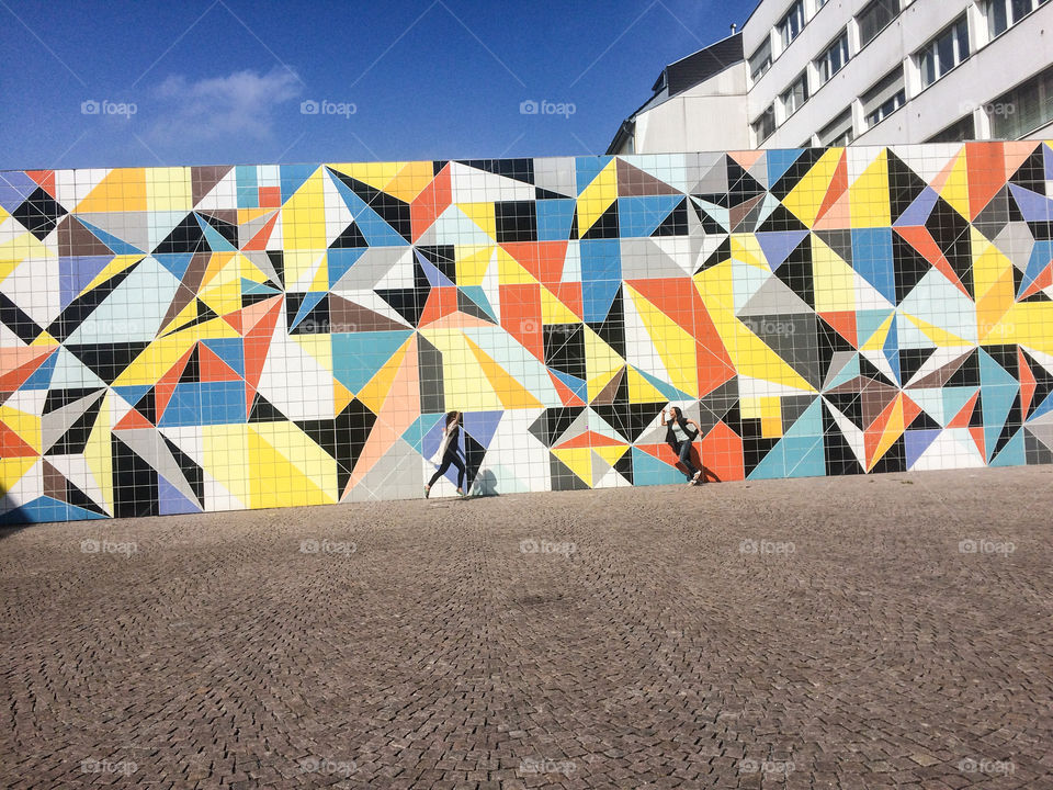 Female friends running in front of colorful tiled wall