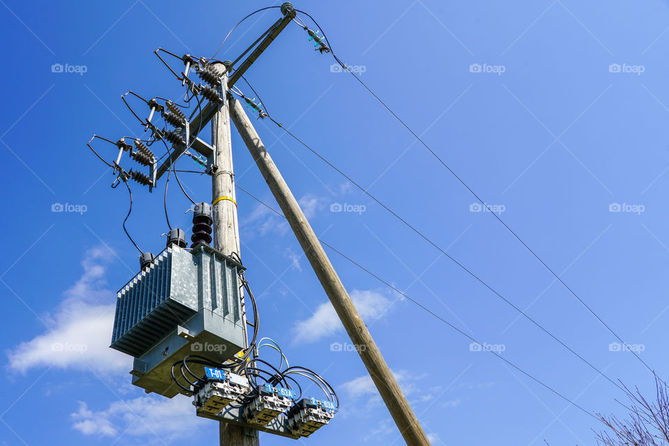 wooden power line pole with electric transformer in rural area against a blue sky