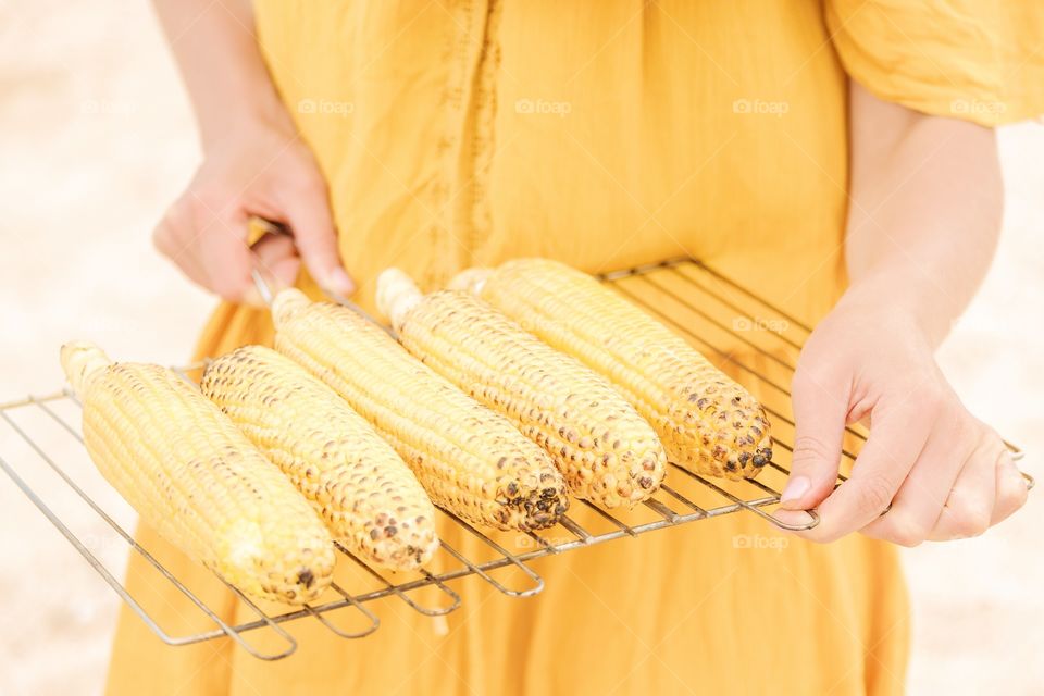 The girl in a yellow dress is holding grilled corn