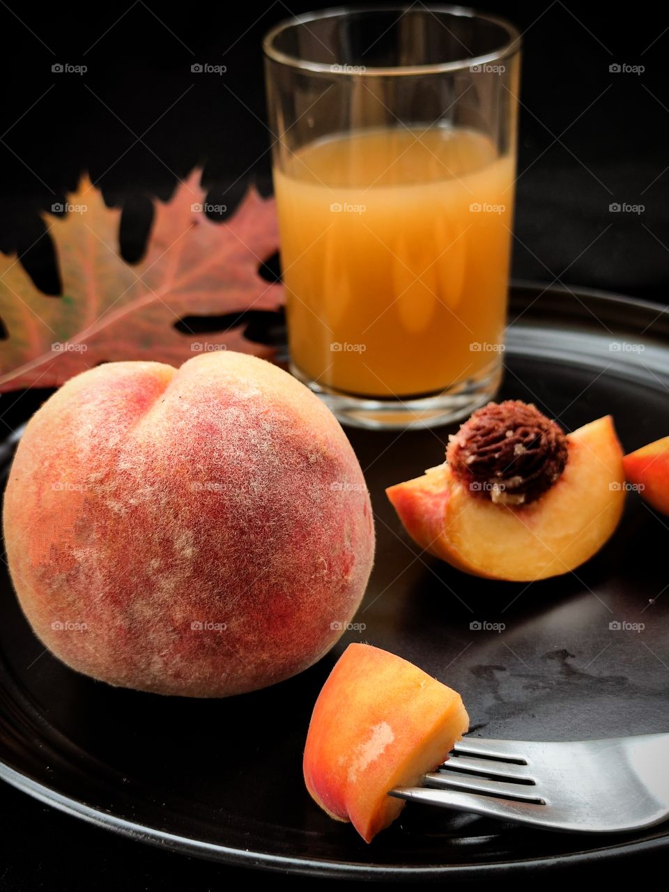 Autumn.  Peach.   A piece of peach on a fork.  A piece of peach with a bone.  A glass with peach juice.  Dark red oak leaf