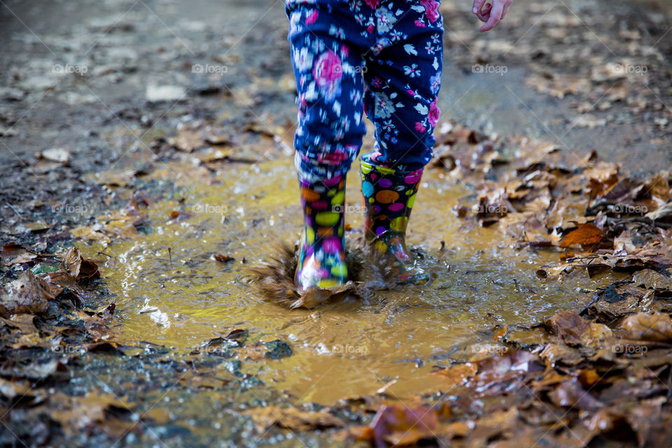 Little girl jumping into mud and water. Summer is about fun, play, being wet and enjoying the outdoors. Bright color boots and vibrant colours with fun and playful feel.