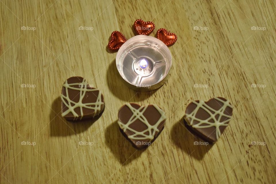 heart shaped valentines day chocolate candies in a flat lay with a candle and shiny red hearts
