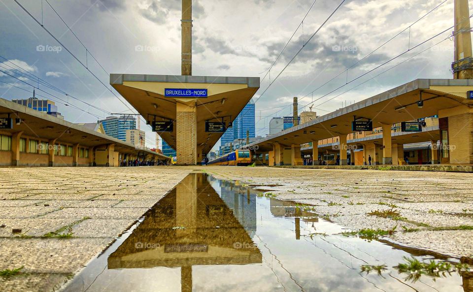 Train on the platform in the railwaystation of Brussels reflected in a puddle after the rain