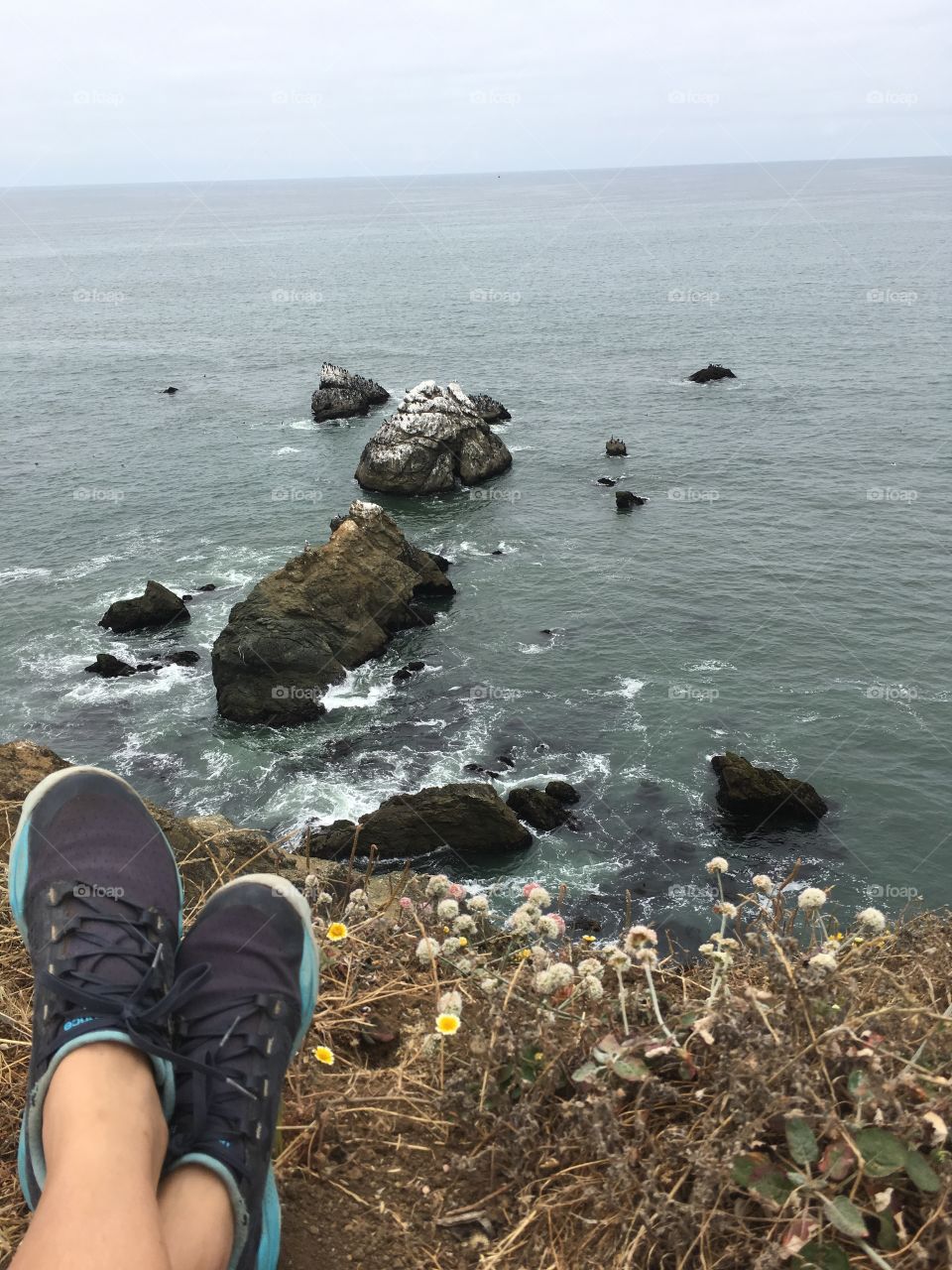 Sitting on a cliff by the ocean with shoes in the frame