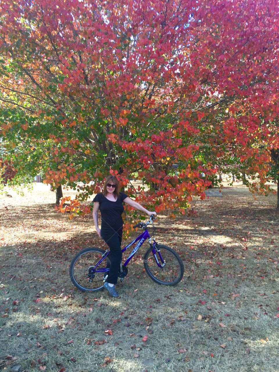 Woman standing with bicycle against autumn tree