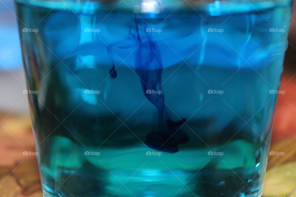 The blue drop of color falling into water changing the waters appearance completely.