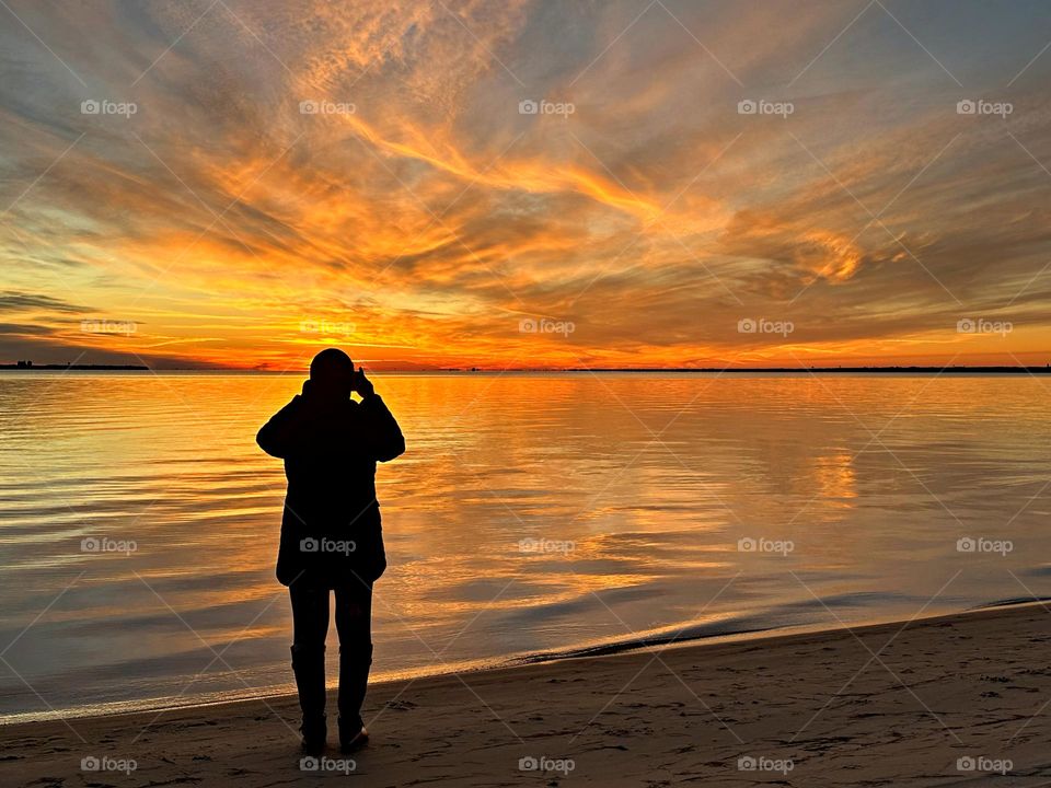 Silhouette of a young lady taking photos of the magnificently colored clouds during sunset