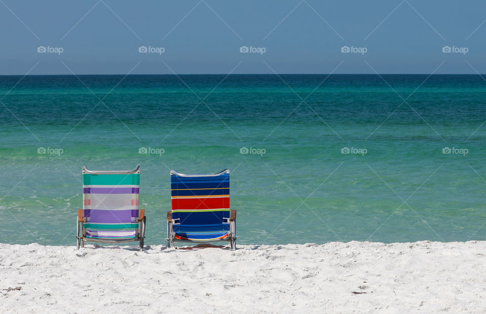 Pair of beach chairs on sugar white Florida beach with emerald colored ocean in the background