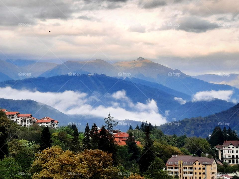 Clouds in mountains, early autumn, moody sky, houses with bright roofs. Rosa Khutor, Sochi, Russia