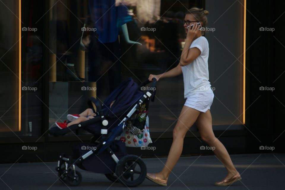 Young Woman With Baby Carriage On A Mobile Phone During Walk