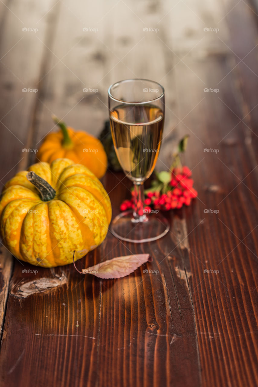a glass of wine on a rustic table, next to pumpkins, leaves and rowan