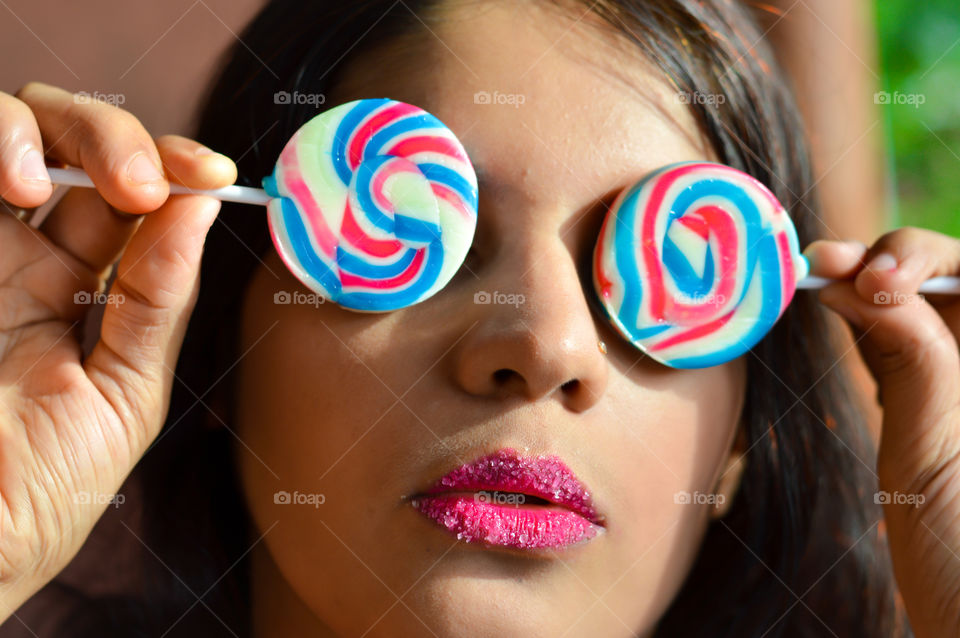 Beautiful woman with sugar coated pink lips, flaunting huge sugary lollipops.
