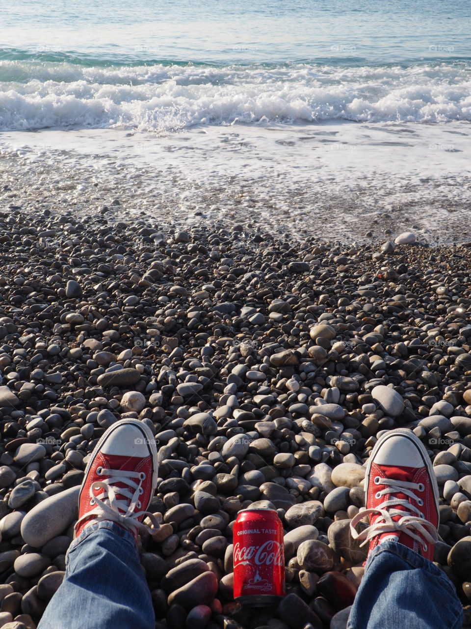 A can of Coca Cola on the beach with red sneakers.