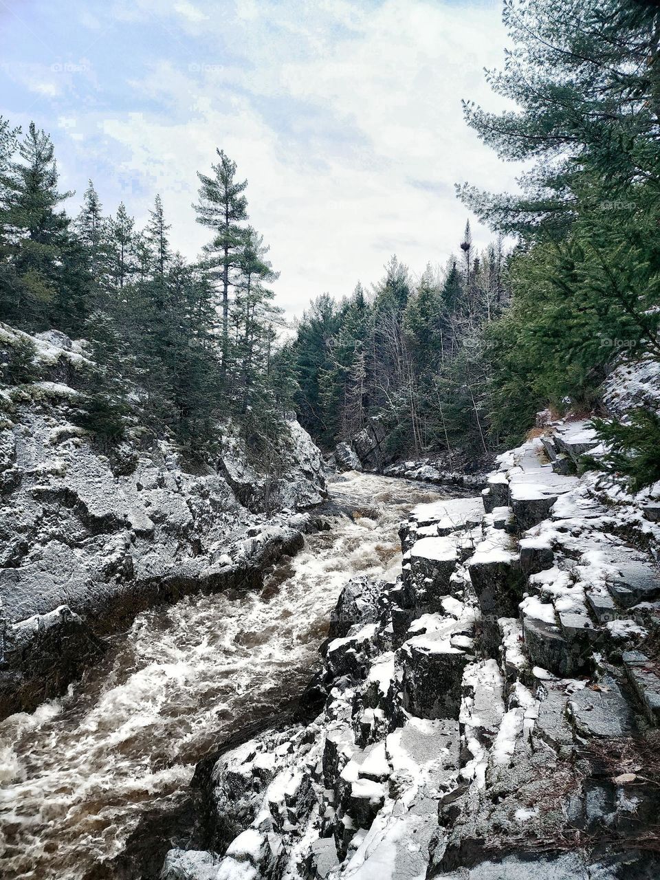 A winter landscape: snow-covered cliffs surrounding a raging river.