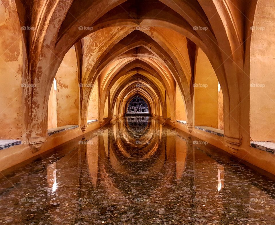 Stunning old baths in Alcazar Palace Sevilla, a golden passage to ancient times. Perfect symmetry and mirroring,  feeling of abundance given by all those coins.