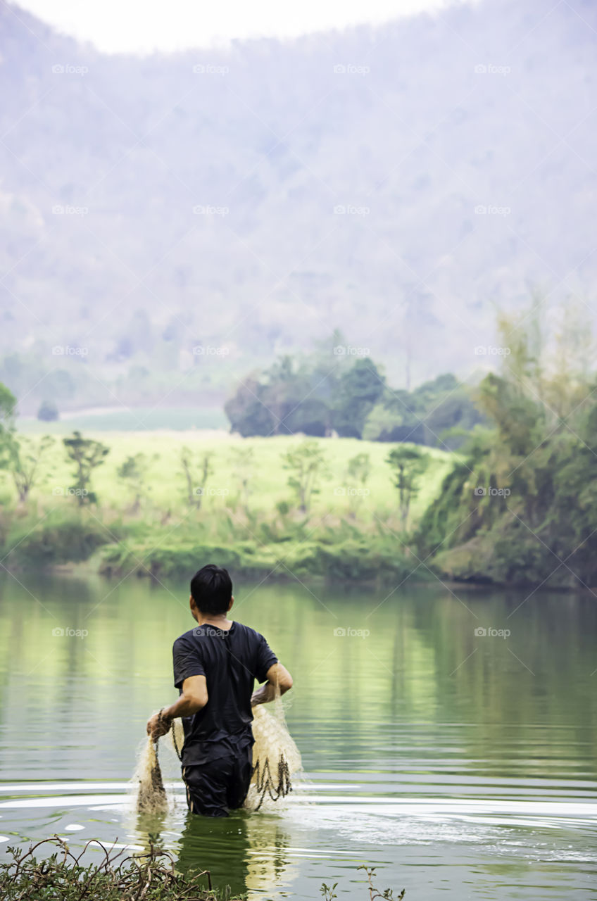 Man holding fishing nets walking in water Background blurred mountains and trees