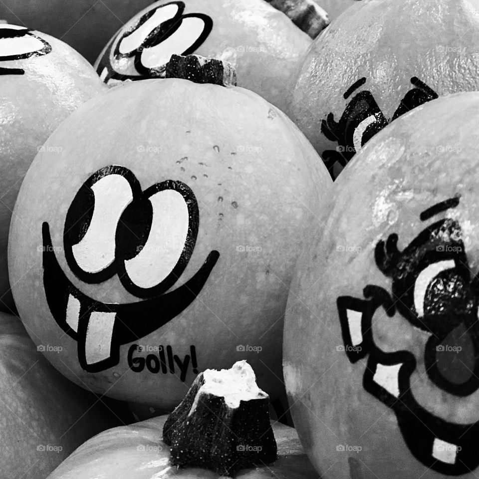 Small pumpkins decorated with goofy hand drawn faces stacked up and ready for fall season. 