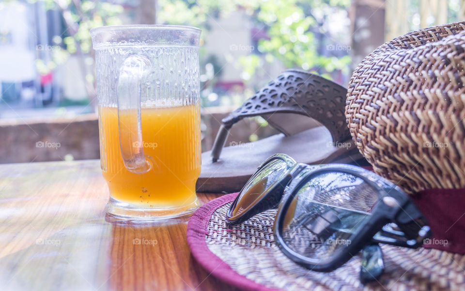 Modern women essential accessories for sunday weekend activities on wooden table. Sunglasses placed over Straw hat, flip flops, with a glass of lime juice with natural sunlight coming from window.
