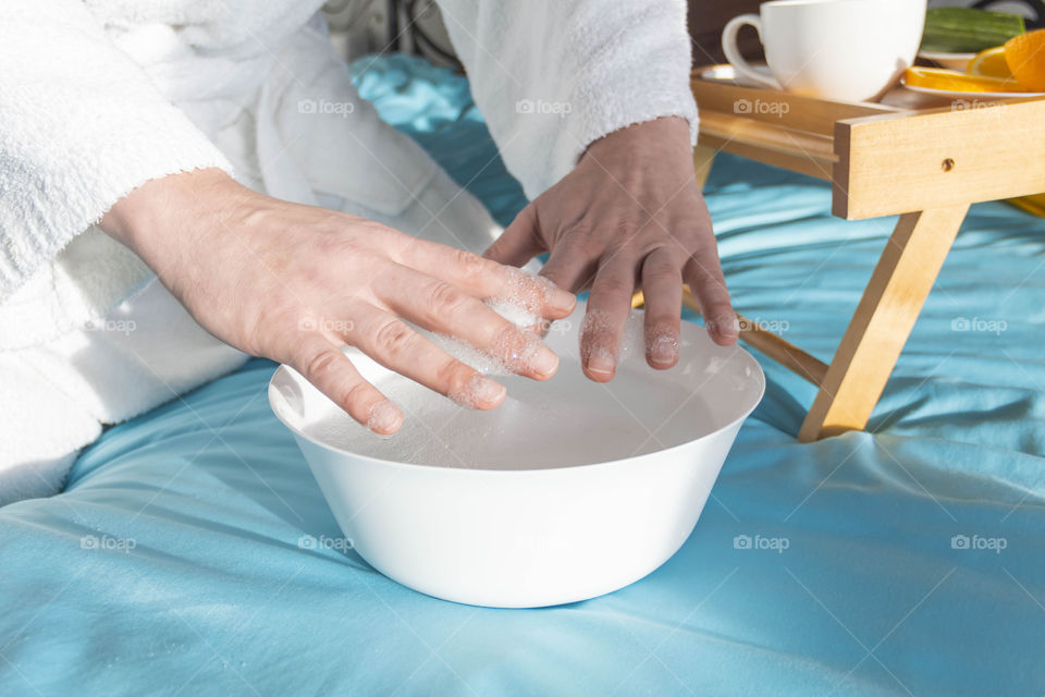 A man at home takes care of himself and does a manicure at home on a blue background and with orange.