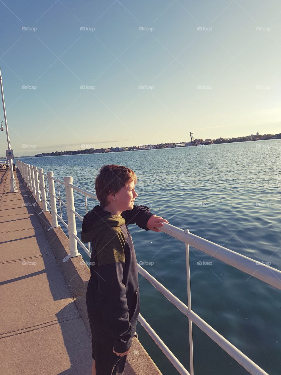 A younge boy looks out on to the water as the sun sets.