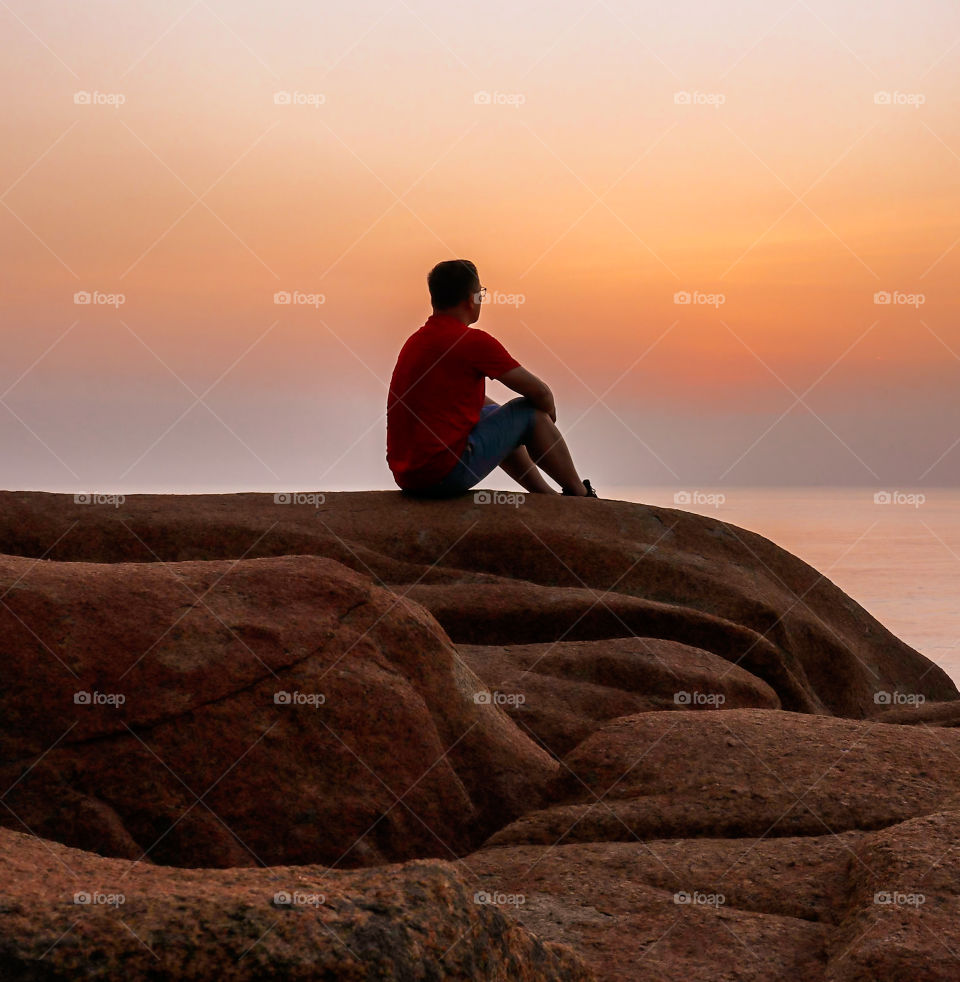 Alone man sitting on a rocks while waiting for the sun to rise.