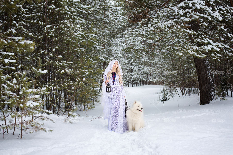 Woman standing on snow with dog holding lantern in hand
