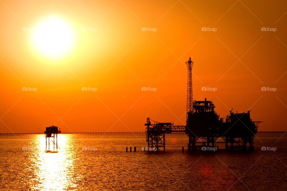 Silhouette of oil platform in sea during sunset