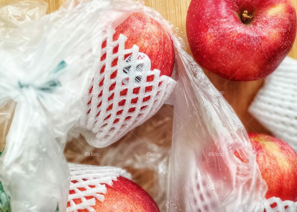 Fresh imported apples from a supermarket come with SINGLE-USE PLASTICS grocery bag and fruit foam net. Environmentalism & Plastic Awareness.