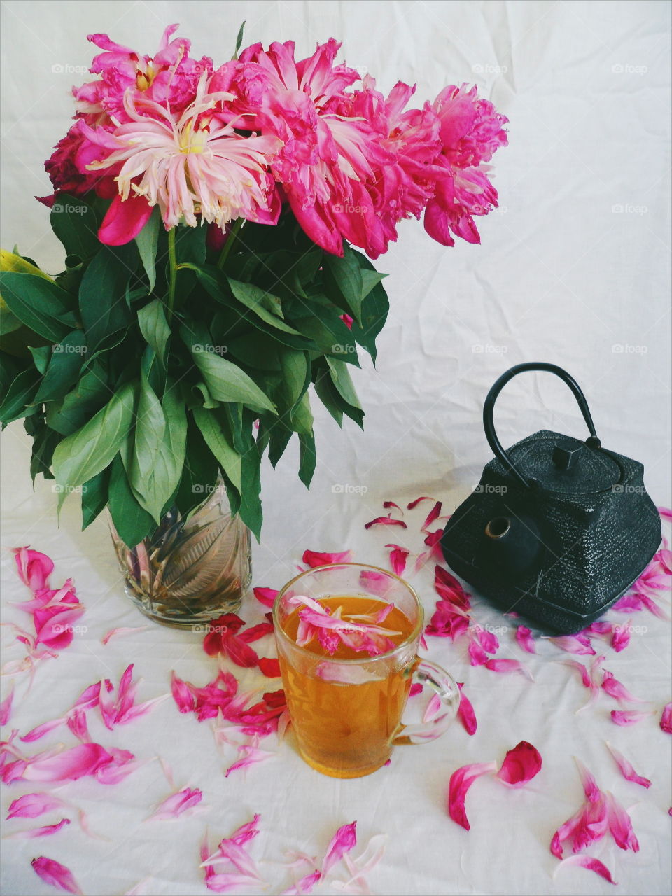 pink bouquet of wilted peony flowers, a cup of green tea and a tea pot