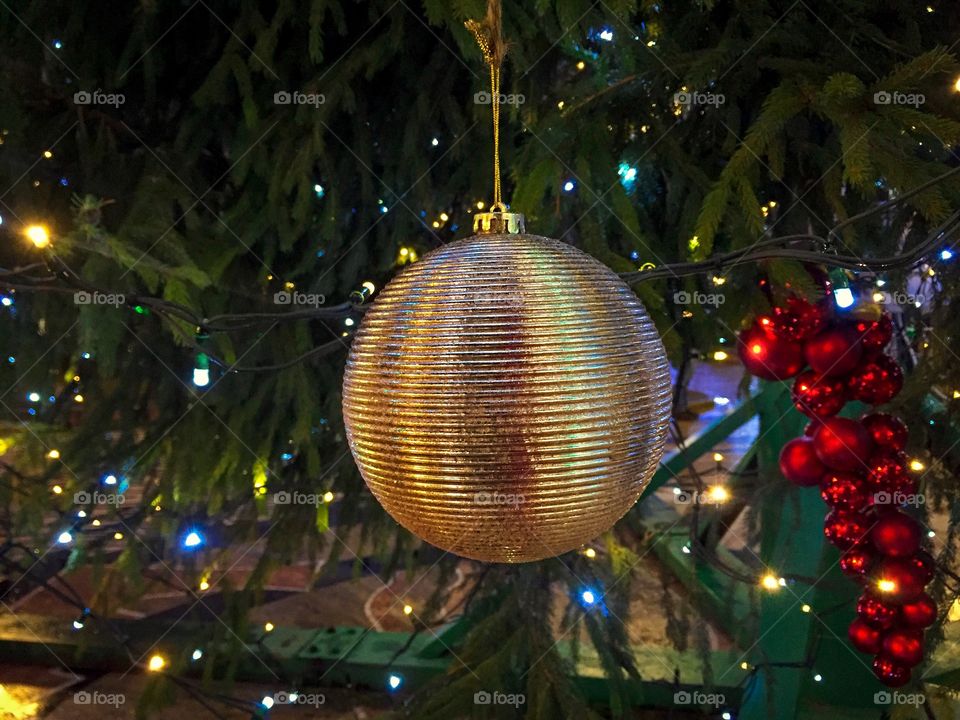 Giant golden Christmas globe hanging on the Christmas tree outside with lights in the background 