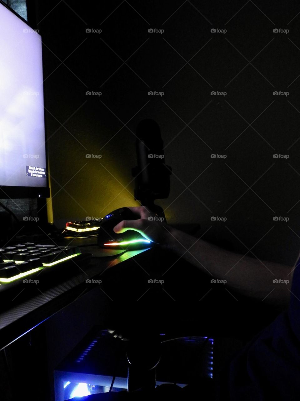 Teenager boy playing Minecraft on the gaming computer seen from his left side and close-up of his hand playing in a dark room.