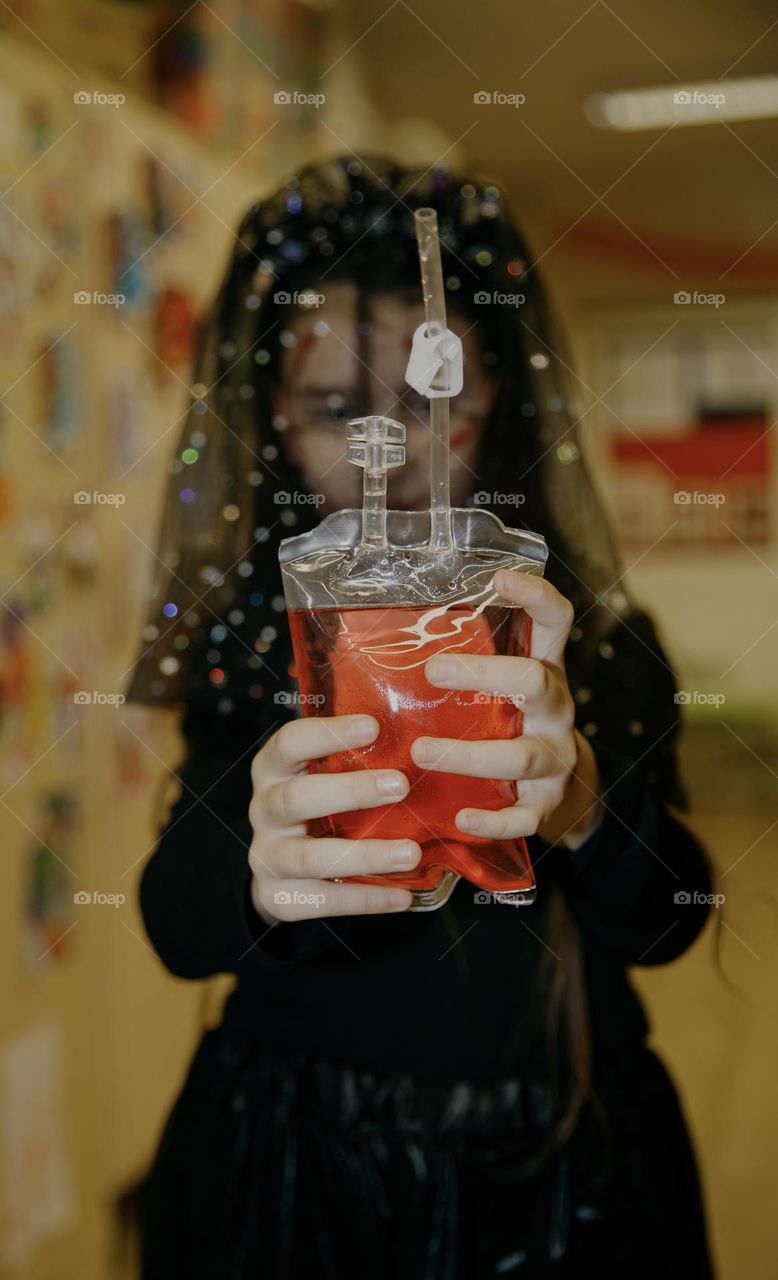 Portrait of one little Caucasian girl in a dead bride costume holding a bag of blood in her hands, close-up side view.