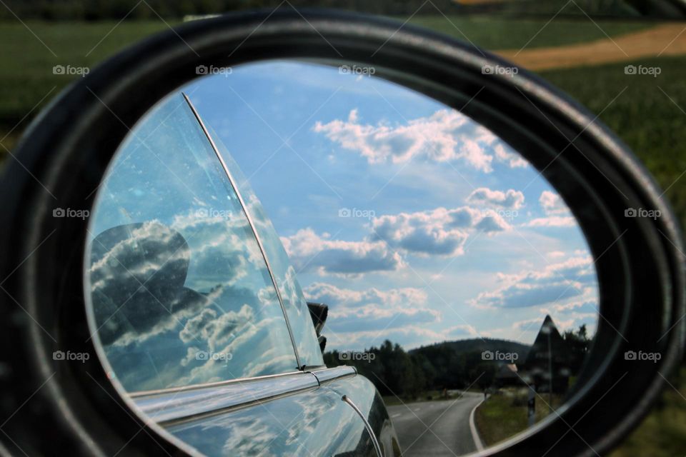 A country road and sky with clouds in the exterior  mirror of a car while driving 