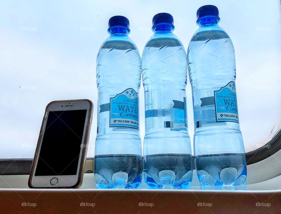 Close up of three bottles of title water and iPhone against the window glass 