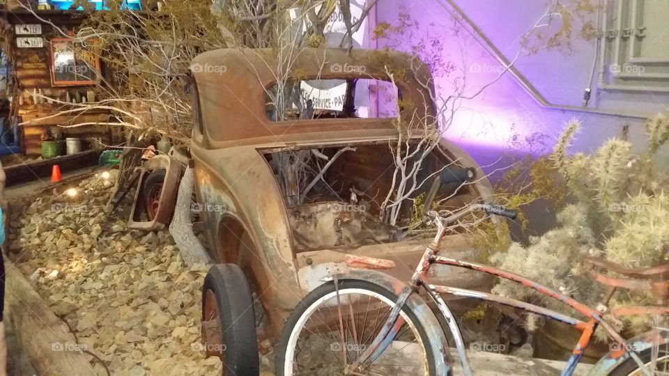 old vehicle with trees growing through it with bike behind it