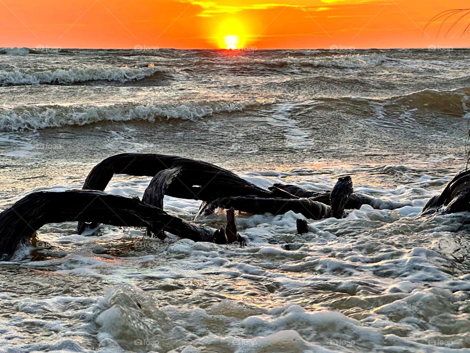 A breathtaking sunset as the waves, often towering and frothy, collide with the shore with great force, sending spray and foam into the air creating a stunning display of energy and motion