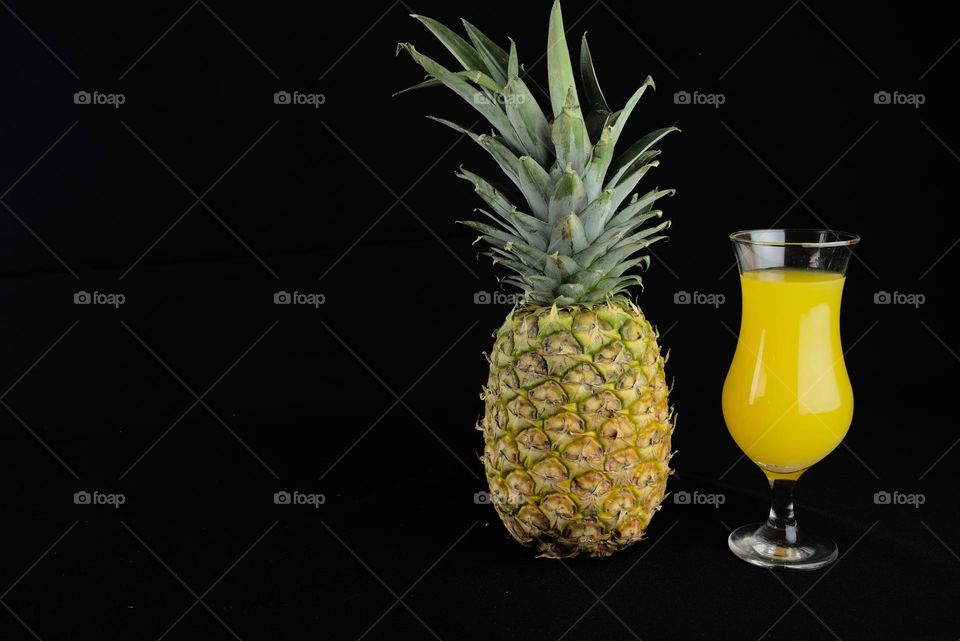 Pineapple and glass cup with natural juice on black background