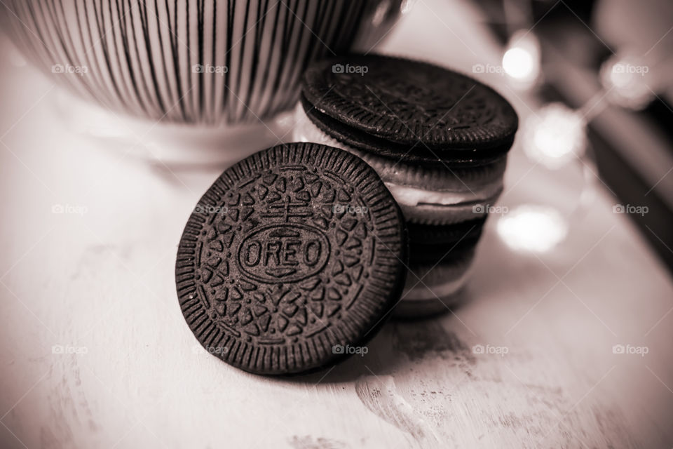 Stack of thin Oreo with cinnamon Oreos on rustic wood with striped bowl and lights in background 