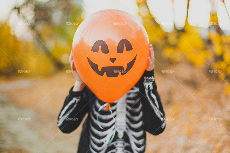 A boy in a skeleton costume holds an orange balloon with a face. Making faces, fooling around.